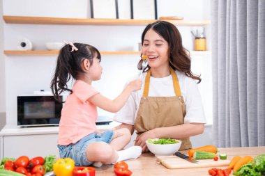 Mutlu bir anne, kızı tarafından parlak, modern bir mutfak ortamında taze ürünlerle besleniyor.