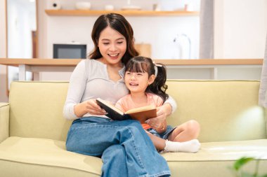 Kadın, gülümseyen bir çocuğa kitap okuyor. Parlak bir odada, bir kanepede. Sevgi dolu bir bağ yaratıyor.