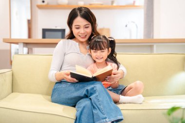 Bir anne, küçük kızına oturma odasındaki kanepede birlikte gülümsüyor.