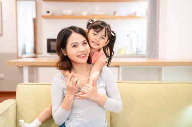 Oturma odası sahnesinde bir kadın ve kızı neşe ve şefkat saçıyor.