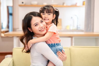 Bir anne genç kızına sevgiyle sarılır. Parlak, modern bir evde. Gülümsemeleri saf sevgiyi yansıtır.