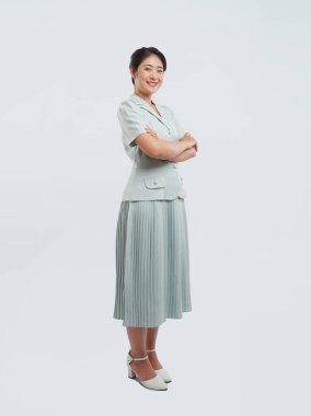 Açık deniz mavisi elbiseli ve beyaz ayakkabılı gülümseyen bir kadın kollarını kavuşturmuş duruyor.