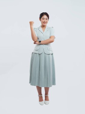 Açık mavi giyinmiş gülümseyen bir kadın, saati ve beyaz ayakkabıları olan bir yumrukla ayakta duruyor.