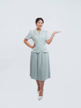 Neşeli bir kadın açık mavi bir takım elbise içinde, plili etekle beyaz bir arka plana karşı poz veriyor.