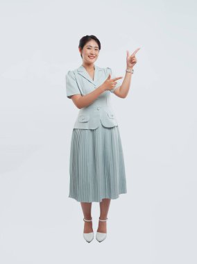 Gülümseyen bir kadın stüdyoda açık renkli bir elbise giyiyor ve sağ üst tarafını işaret ediyor.