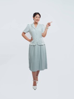 Genç bir kadın, açık mavi bir takım elbise ve beyaz bir arka planda katlanmış bir etek giyiyor.