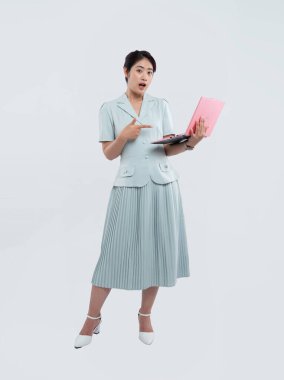 Genç bir kadın pembe bir dizüstü bilgisayarı işaret ediyor. Yüzünde mavi bir takım elbise ve topuklu ayakkabı var.