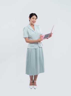 Açık mavi takım elbiseli bir kadın pembe bir dizüstü bilgisayar tutuyor. Beyaz bir arka planla parlak bir stüdyoda.