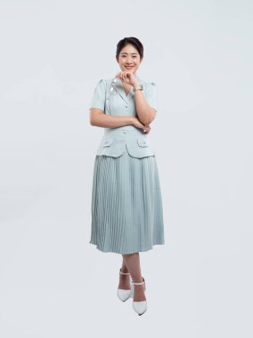 Açık yeşil etek ve bluz giymiş, poz veren çekici Asyalı bir kadının stüdyo fotoğrafı.