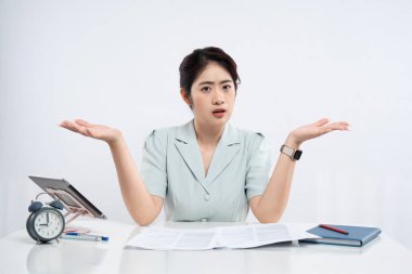 Masasında açık renkli bir ofiste oturan bir kadın. Elinde evrak saati tableti var. Kafası karışmış görünüyor.