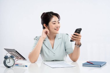 Açık mavi elbiseli gülümseyen bir kadın parlak bir masada oturuyor ve modern ofis atmosferini kullanıyor.