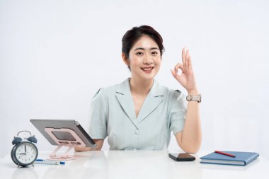 Bir kadın tablet defterinin önünde gülümser telefon ve çalar saat çalar ve tamam el hareketi yapar.