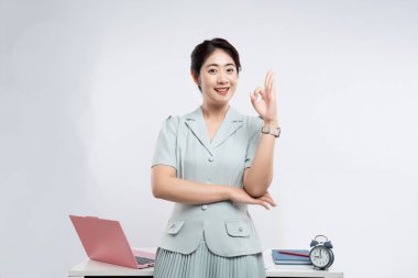 Açık yeşil takım elbiseli gülümseyen kadın masasında düz beyaz bir arka plana karşı 