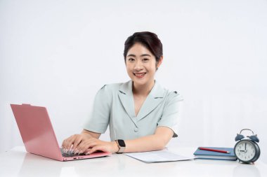 Masada dizüstü bilgisayar kullanan bir kadın oturuyor. Parlak, modern bir ofis ortamında.