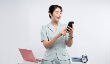 Takım elbiseli gülümseyen bir kadın ofis ortamında oturan akıllı telefonuyla iletişim kurar.