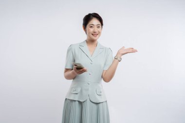 Açık deniz mavisi kıyafetli bir kadın bir elinde telefonu tutarken gülümsüyor ve dışa doğru hareket ediyor.