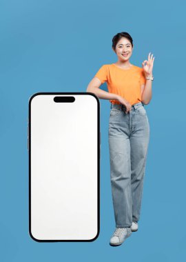 Gülümseyen bir kadın mavi arka planda büyük boş bir akıllı telefona yaslanır ve 