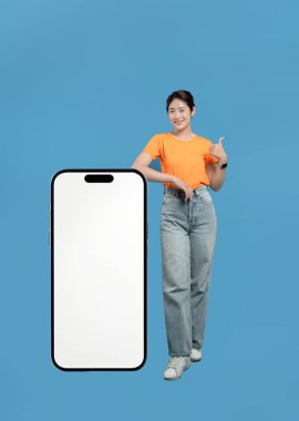 Gülümseyen genç bir kadın, beyaz ekranlı büyük bir akıllı telefonun yanında baş parmağını kaldırıyor.