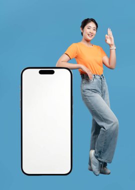 Genç bir kadın, parlak beyaz bir ekranı gösteren büyük bir akıllı telefona yaslanıyor.