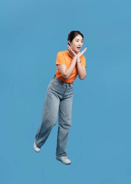 Genç bir kadın mavi bir arkaplanda şaşkın şaşkın bakıyor ve günlük kıyafetler giyiyor.