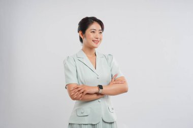 Zarif genç bir kadın, stüdyoda profesyonel yeşil bir kıyafetle kollarını kavuştururken özgüvenle gülümsüyor.