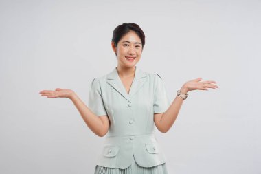 Açık yeşil takım elbiseli gülümseyen Asyalı bir kadın stüdyo ortamında avuç içi açık bir şey sunar.