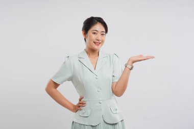 Açık yeşil takım elbiseli, gülümseyen bir kadın. Eli açık, sanki havada bir nesne sunuyormuş gibi.