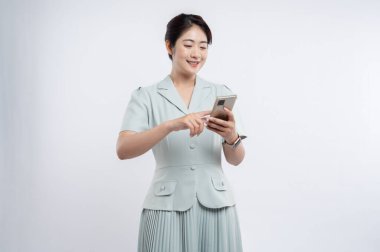 Asyalı bir kadın cep telefonunu kullanırken eski bir takım elbiseyle arka planda duruyor.