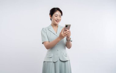 Asyalı bir kadının şık, soluk yeşil etekli fotoğrafında. Telefona bakıyor. Basit, parlak modern.