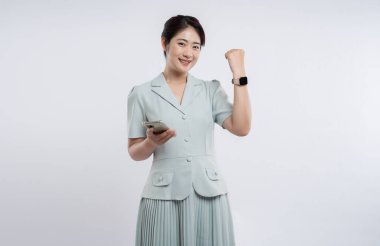 Açık mavi elbiseli neşeli bir kadın telefonla gülümsüyor ve zafere yumruk atıyor.