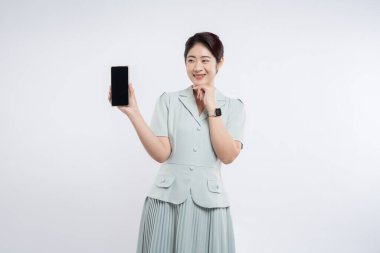 Açık yeşil elbiseli gülümseyen bir kadın elinde boş ekranlı akıllı bir telefon tutuyor.