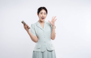 Resmi giyinmiş genç bir kadın, beyaz bir arka fona akıllı telefon tutarken şaşırır.