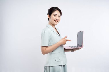 Açık yeşil takım elbise giyen bir kadın pembe dizüstü bilgisayarını beyaz arka plana doğru sunarken gülümsüyor.