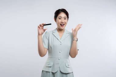 Gülümseyen Asyalı bir kadın bir kredi kartı tutuyor ve satın alma konusunda heyecanlıymış gibi elini kaldırıyor.