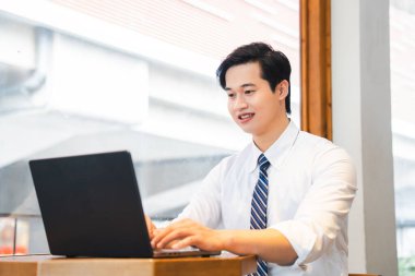 Odaklanmış bir adam dizüstü bilgisayarıyla çalışır. Kravat takar ve parlak ışığı olan bir pencerenin yanına oturur.