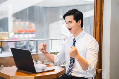 Beyaz gömlekli bir adam bir kafede kutluyor. Yumruklarını sıkarak dizüstü bilgisayarına bakıyor.