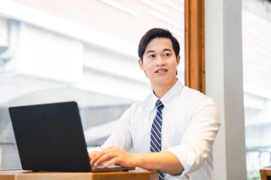 Genç bir Asyalı dizüstü bilgisayarı başında gömlek ve kravat takıyor. Memnun ve profesyonel görünüyor.