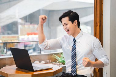 Genç bir profesyonel, başarılı bir jest yaparak masasında sevinçle yumruğunu kaldırır.