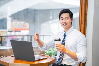 Beyaz gömlekli ve çizgili kravatlı genç profesyonel bir adam laptopuyla kahve içiyordu.