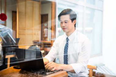 Beyaz gömlekli ve kravatlı profesyonel bir adam parlak ışıklı kafede özenle çalışıyor.