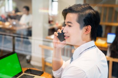 Cam pencerenin yanındaki masada uzaktan çalışan gömlekli bir adam cep telefonuyla konuşuyor.