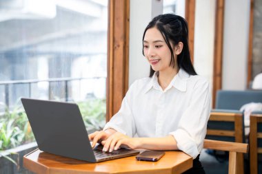 Kafede dizüstü bilgisayar kullanan bir kadın modern bir çalışma ortamının keyfini çıkarıyor.