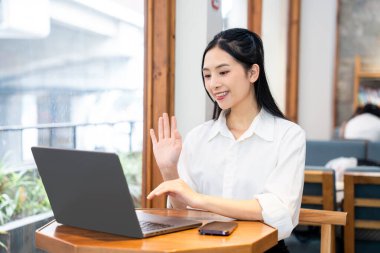 Bir kadın, parlak bir kafedeki masada otururken bilgisayarını kullanıyor.