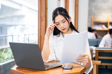 Genç bir kadın bir kafede çalışıyor. Düşünceli bir ifadeyle gazeteye bakıyor.