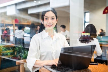 Kafede dizüstü bilgisayarıyla çalışan genç bir kadın.