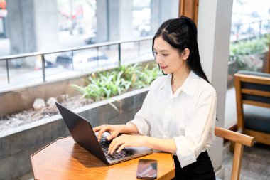 Bir kadın bir kafede oturmuş laptopuyla yazı yazıyor. İşine odaklanmış ve meşgul görünüyor.