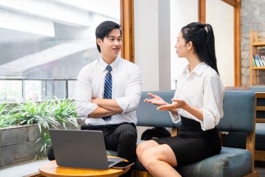 Ofisteki iş adamları iyi aydınlatılmış gayri resmi bir ortamda dizüstü bilgisayarın yanında sohbet ediyorlar.