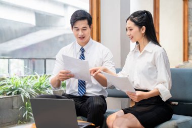 Profesyonel kıyafetli bir adam ve bir kadın birlikte otururken kağıt belgelere bakıyorlar.