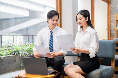 İki meslektaş, modern bir ofiste, takım çalışmasını teşvik etme ve olumlu bir çalışma alanı oluşturma konularını tartışıyor.