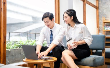 Bir kadın ve bir erkek, elinde kahve bardağıyla, parlak bir çalışma alanında dizüstü bilgisayarda birlikte çalışırlar.